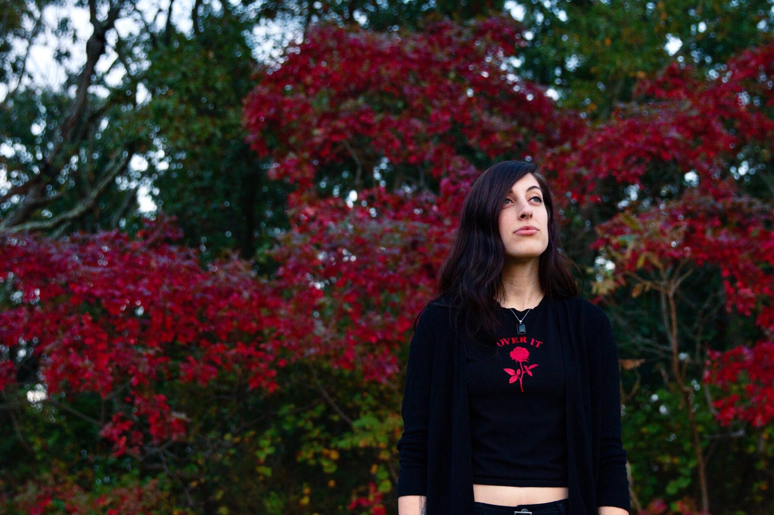 Morgan Mandriota standing in front of red and green trees by Georgina Berbari